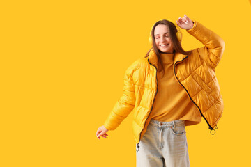 Beautiful young woman in stylish warm clothes and headphones on yellow background