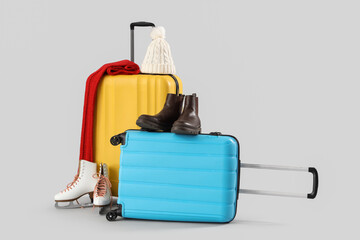 Suitcase with winter accessories and ice skates on light background