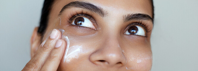 Beauty close-up south asian woman skincare portrait, one hand gently touching the face and applying a cream swatch or skin care cosmetic mask, facial hydration.