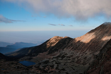 Dramatic mountain landscape at sunrise.  A serene lake nestled in a rugged valley, bathed in golden light. Breathtaking scenery perfect for travel, adventure, and nature themes.