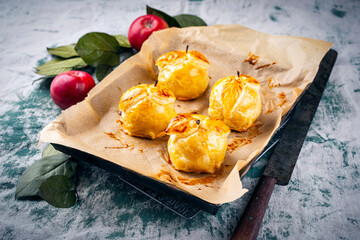 Traditional baked apples coated in pastry, decorated with pastry leaves and served as a close-up on a baking tray with baking paper