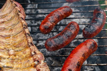 pork ribs and pork sausages called chorizos grilling on the grill, background for summer gastronomy concept