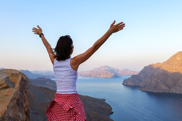 woman admires the panoramic view of the Musandam fjords from a rocky cliff at sunset, Khor Najd, Oman