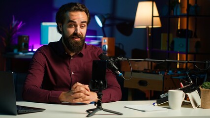 Media star talking in front on smartphone attached to tripod stabilizer in studio, discussing with viewers. Man using mobile phone to record video in living room for social media, camera A