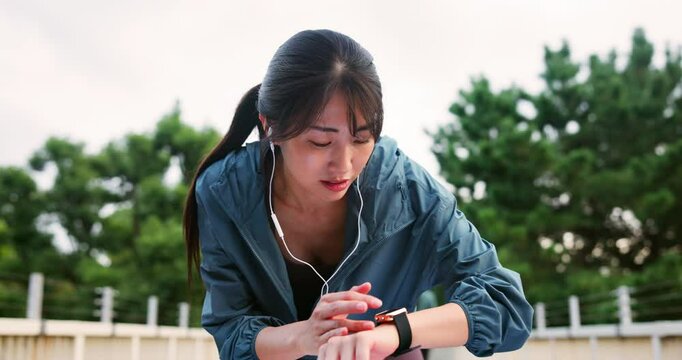 Woman, watch and exhausted athlete in city, check stats and earphones for sports music or cardio. Female person, monitor time and tired runner in Japan, fitness tracker and training exercise results