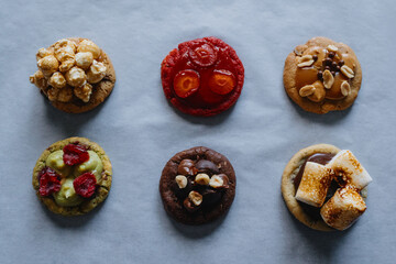 Collection of homemade round cookies with different toppings - raspberry, strawberry, pistachio, caramel, chocolate, peanuts, marshmallow, popcorn. 