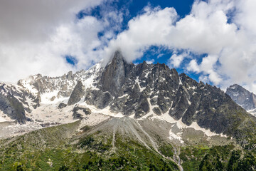 Petit Dru granite mountain wall and summit in Chamonix valley, french Alps. Prominent mountain peak in the Alps, stunning landscape view of the rocky peak covered with clouds, snow and ice