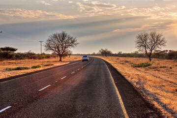 african road highway at sunset perspective, car far away dry land outback