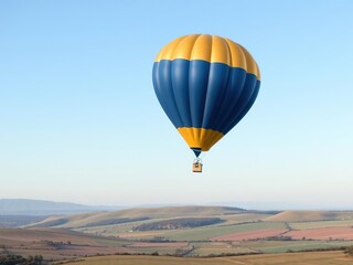 Obraz premium A beautiful blue and gold flying balloon is seen sailing above a peaceful landscape of rolling hills and fields with a light blue sky overhead, light blue sky, blue balloon, gentle movement