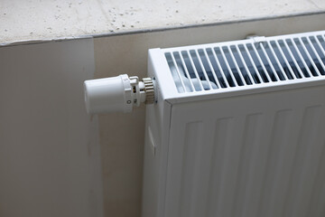 Modern white radiator with adjustable thermostatic valve installed near window sill in bright room...