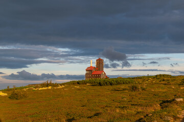 Słońce oświetla budynek dawnego schroniska przy Śnieżnych Kotłach w polskich Karkonoszach tuż przed zachodem słońca