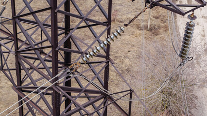 High -voltage transmission lines with a metal rusty fastening suspension system of wires and connecting insulators on a blurred background of fields and trees.