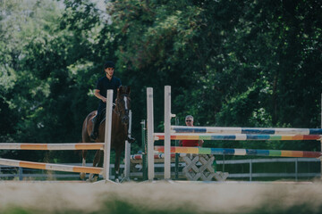 A young equestrian competes in an outdoor horse jumping event, showcasing skills and concentration....