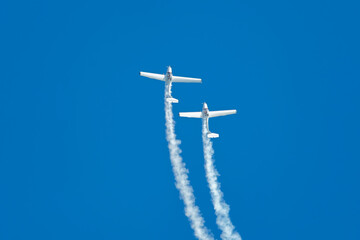 Stunt aerobatic plane performing stunts in blue sky with smoke trail. Concept of teamwork, collaboration, coordination, trust, precision, difficulty, challenge, speed, synergy