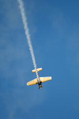 Golden stunt aerobatic plane performing stunts in blue sky with smoke trail. Concept of speed, difficulty, precision, risk