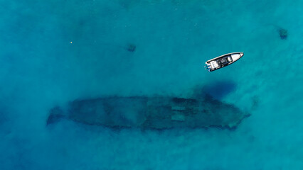 A sports boat is anchored in the middle of the sea with turquoise water from the top view of a drone