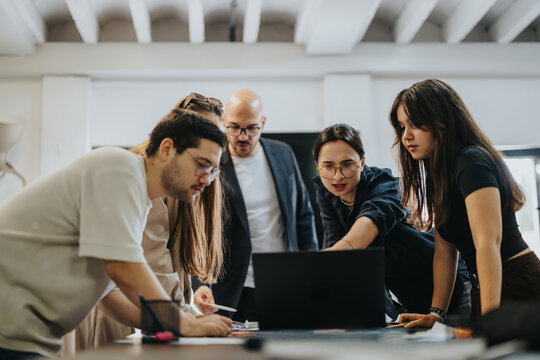 A diverse group of students actively collaborating on a project with their professor providing guidance. The image captures teamwork, support, and academic engagement in a classroom setting.