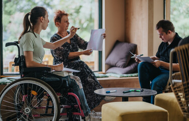 A group of diverse individuals, including someone in a wheelchair, engaged in a collaborative meeting in a cozy room setting. They are actively sharing and discussing ideas.