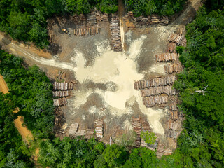 Aerial view of a logging yard in the Amazon rainforest: The yard is located in a clearing surrounded by dense forest. The logs are stacked in neat rows, and they are a variety of sizes and species.