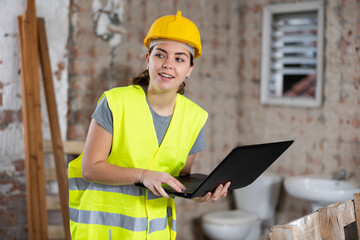 Fototapeta premium Woman construction worker standing and using laptop in building site.