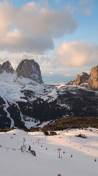 View of a ski resort piste with people skiing in Dolomites in Italy. Ski area Belvedere on sumset. Canazei, Italy. Horizontal camera pan