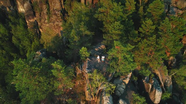 Aerial view of two people on a rocky cliff surrounded by dense green forest trees. Hikers standing on a rock, capturing the essence of nature and exploration.