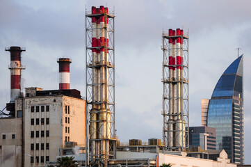 Industrial chimneys with modern skyline highlight industry vs urban development.