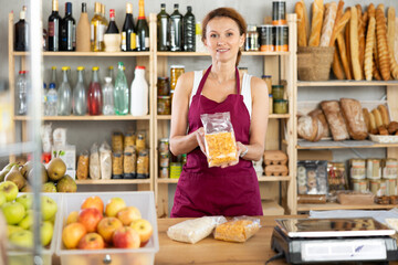 Friendly female salesperson offers to buy oat flakes and cornflakes in produce section of a supermarket
