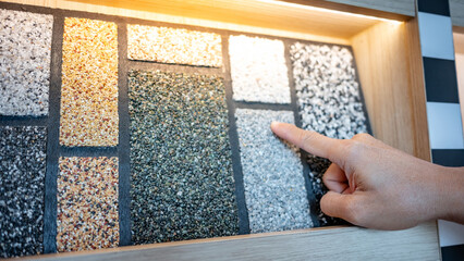 Washed gravel flooring design concept. Architect hand pointing at wash gravel texture on display shelf in material showroom. Choosing exterior floor finishing for non slippery area