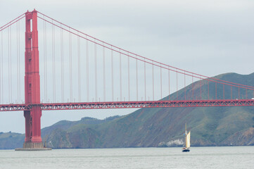 Sailboat under red bridge with misty hills, symbolizing coastal serenity