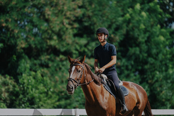 A young equestrian is seen confidently riding a horse through a lush, green landscape, showcasing a...
