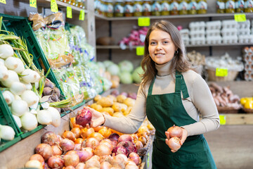 Female seller working in supermarket and lays out fresh onions on counter