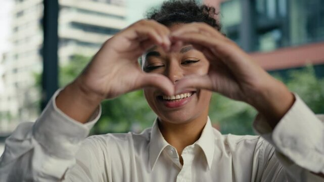 Close up face happy African American woman showing sign gesture joined fingers frame heart shape smile love female girl businesswoman startup work business city outdoors loving feelings support hands