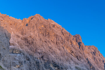 Sunset in the mountains. Red and orange burning sky horizon behind the alpine mountain range. Rocky mountain peaks of the Dolomites at sunset and dawn at sunrise light sunrays going through the clouds
