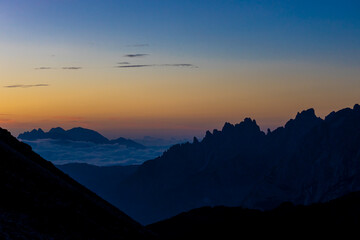 Sunset in the mountains. Red and orange burning sky horizon behind the alpine mountain range. Rocky mountain peaks of the Dolomites at sunset and dawn at sunrise light sunrays going through the clouds