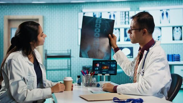 Indian healthcare expert sharing medical expertise with a patient in office, reviewing x ray scans and MRI diagnostics to focus on accurate treatment and recovery. Insurance consultation. Camera B.