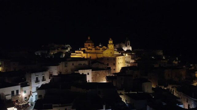 Vis&atilde;o a&eacute;rea noturna do castelo na cidade de Ostuni, It&aacute;lia. O castelo iluminado destaca-se contra o c&eacute;u noturno, revelando a arquitetura medieval e a atmosfera encantadora da cidade