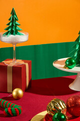 Christmas advertisement photo with colorful ornaments by paper and wool. Empty space in center of red table for product displaying, green and orange background