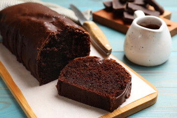 Tasty chocolate sponge cake on light blue wooden table, closeup