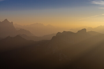 Sunset in the mountains. Red and orange burning sky horizon behind the alpine mountain range. Rocky mountain peaks of the Dolomites at sunset and dawn at sunrise light sunrays going through the clouds