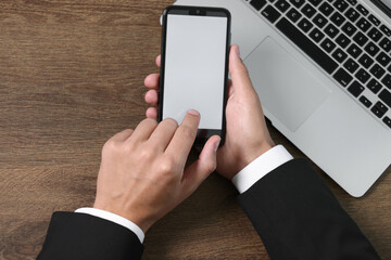 Man unlocking smartphone with fingerprint scanner near laptop at wooden table, top view