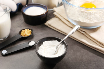 Baking powder and spoon in bowl on grey textured table