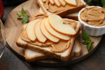 Tasty sandwiches with peanut butter, apple and mint on wooden table, closeup