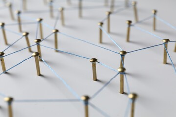 Network connection. Nails linked together by thread on white table, closeup