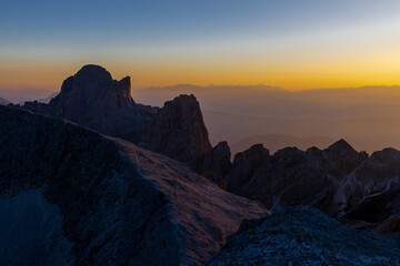 Sunset in the mountains. Red and orange burning sky horizon behind the alpine mountain range. Rocky mountain peaks of the Dolomites at sunset and dawn at sunrise light sunrays going through the clouds