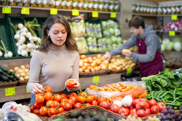 Pleased young female buyer purchasing tomatoes in grocery store with large assortment