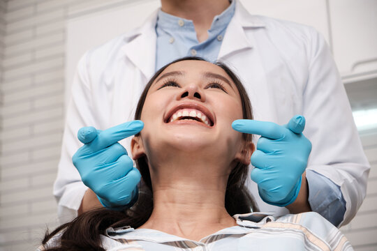 Close-up shot of beautiful Asian female face, white teeth, and cheerful face in dentist's hand, dental treatment with tooth whitening and cleaning in doctor hospital clinic, oral hygiene healthcare.