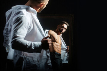 Fashion male model with hot naked body in white shirt. A sexy man in an unbuttoned white shirt on black background. Handsome muscular man with naked torso and shirt. Guy with with open shirt.