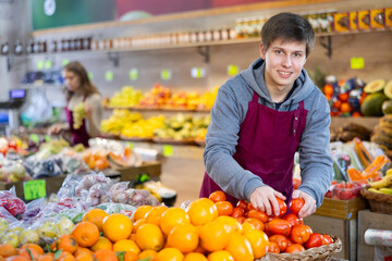 Salesman in an apron puts ripe tomatoes on a supermarket window