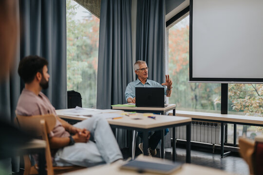 A group of students attentively listening to an elderly professor in a bright, modern classroom. The atmosphere is focused and educational, highlighting a learning environment.